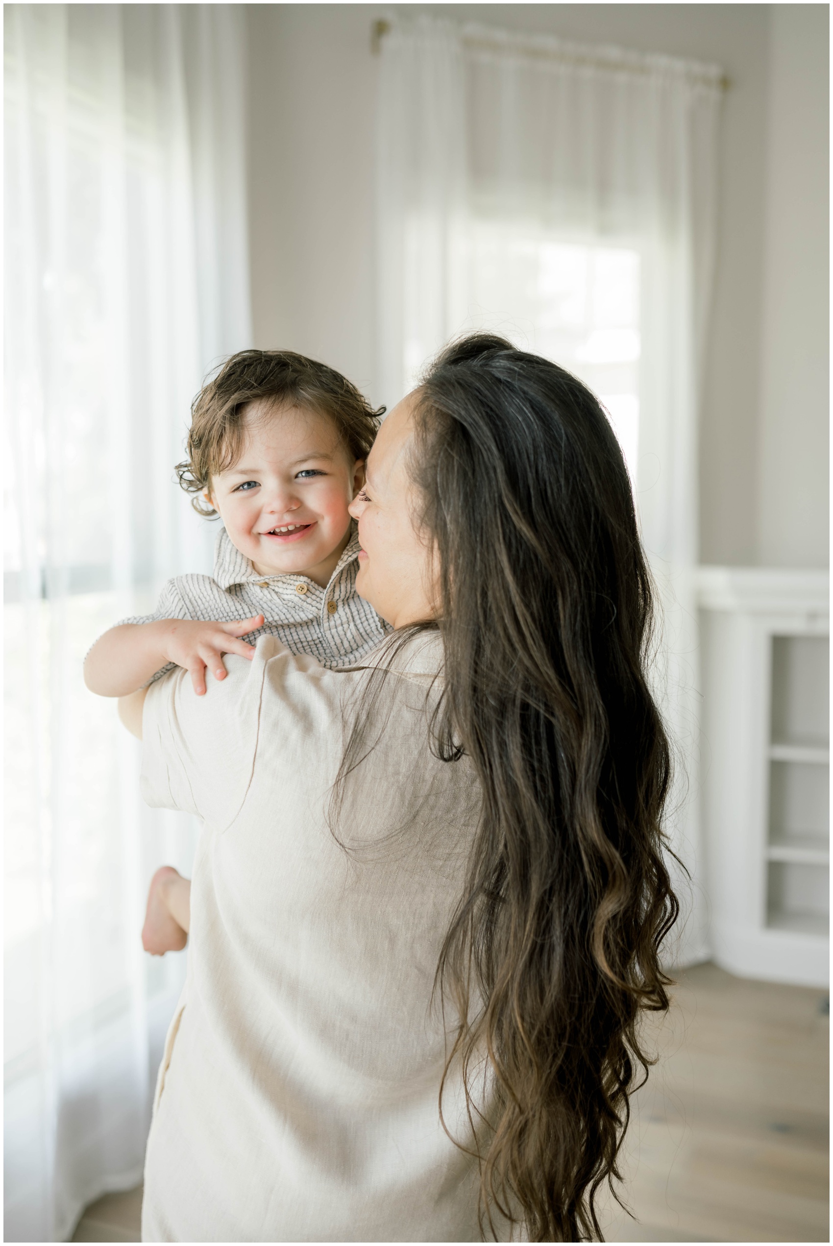 A happy toddler smiles in mom's arms while standing in a studio before visiting trampoline parks in okc