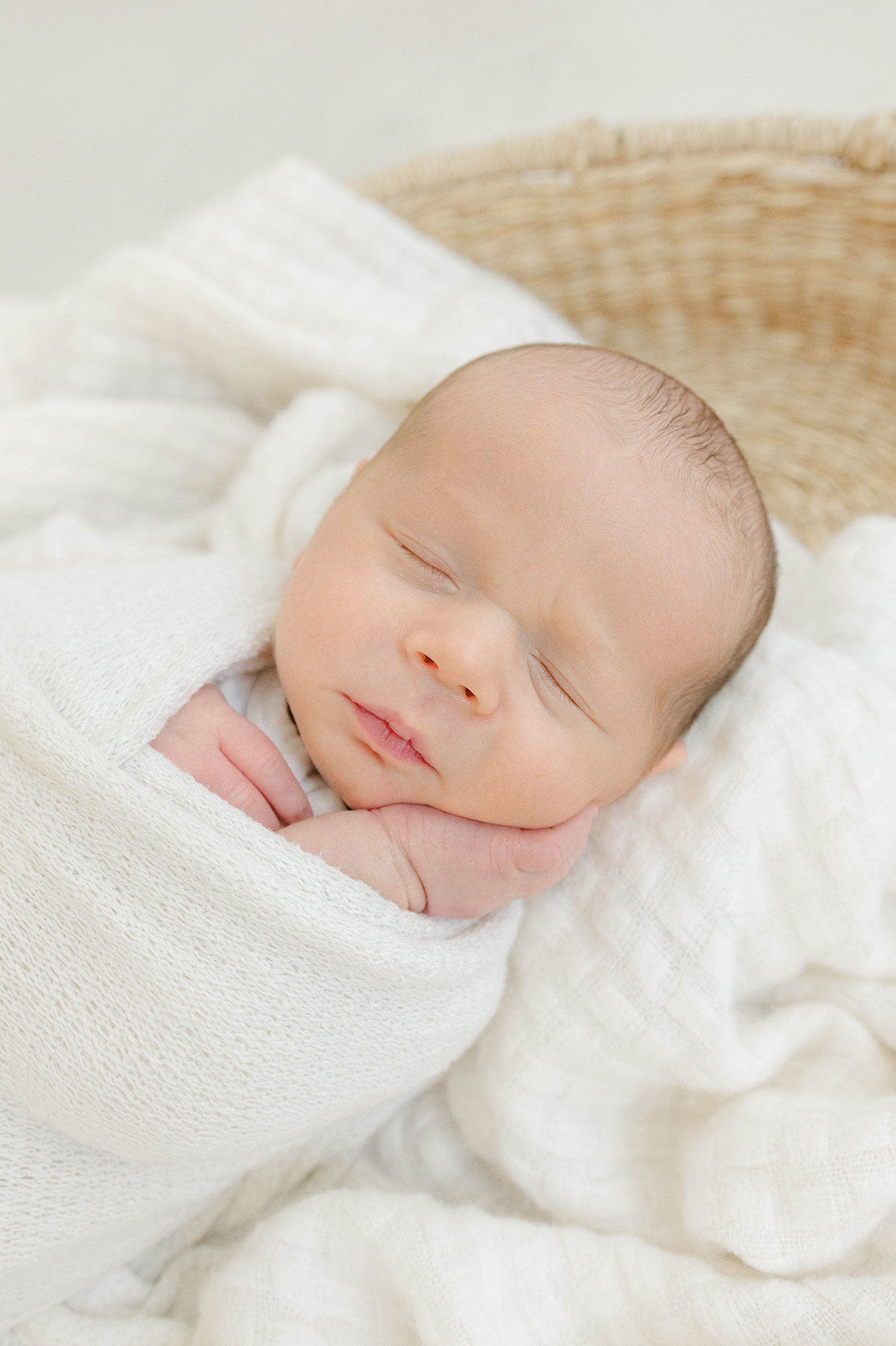 A newborn sleeps in a white swaddle in a woven basket thanks to willow birth services